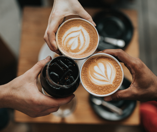 is coffee good for us photo of 3 hands holding different variations of coffee drinks.