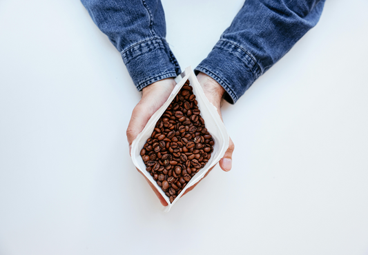 Robusta or Arabica? A man holds an open bag of coffee beans over a white counter.