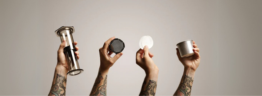 Image for 'how to use aeropress' which shows four hands holding up different parts of an aeropress brewer against a cream background.