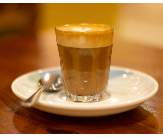 a photo of a small milk based coffee in a glass, on a saucer to answer the question what is a piccolo coffee.