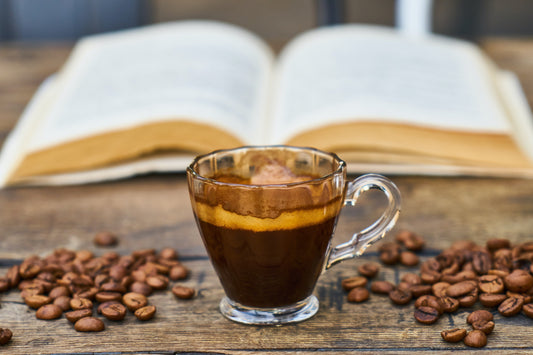 A glass cup of cold brew coffee sitting on a bench in front of an open book.