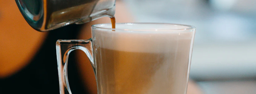 Close up of a Spanish latte being made in a glass coffee mug.
